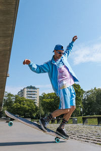 Fashionable young man longboard skating on overpass road under blue sky