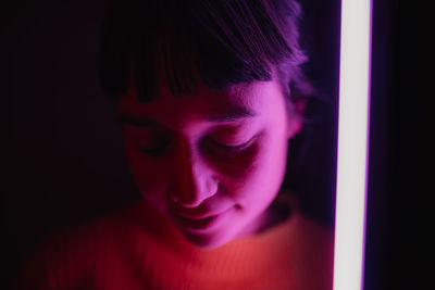 Close-up of woman by illuminated lighting equipment in darkroom