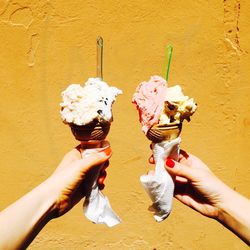 View of person holding ice cream cone in front of wall