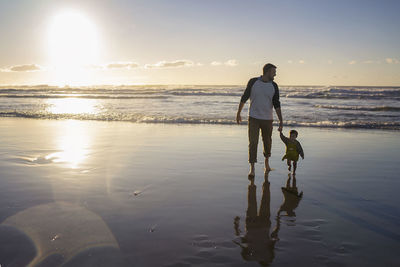 Rear view of woman standing at beach during sunset