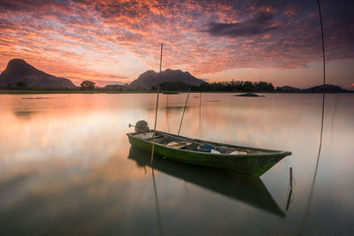 Boat moored in lake against sky during sunset