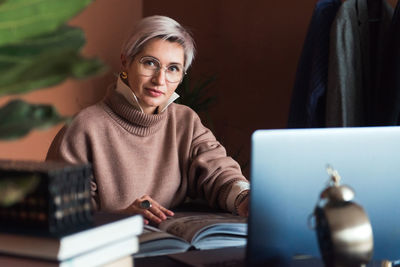 Fashion woman in brown oversize sweater working in modern work place or office with laptop