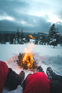 Low section of couple on snow covered land by fire 