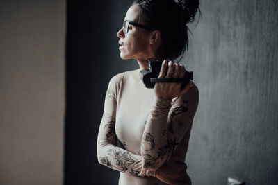 Woman looking away while standing against wall