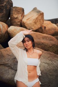 Portrait of sensuous young woman wearing bikini standing against rocks
