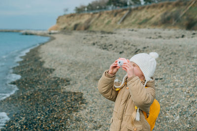A little girl squinting photographs the autumn seascape on a childrens pink camera. the child