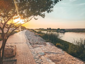 Footpath by lake against sky during sunset