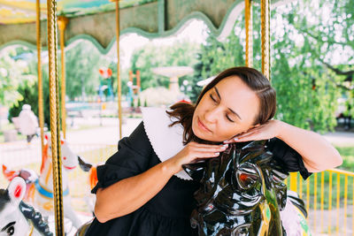 Beautiful brunette girl in a black dress poses on a bright carousel with horses