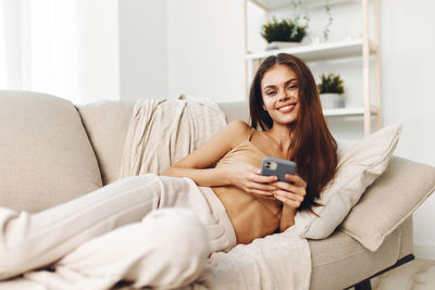 Young woman using phone while sitting on sofa at home