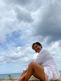 Woman sitting on beach against sky