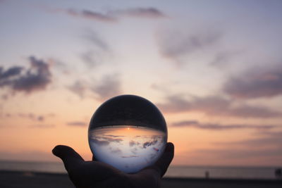 Person holding ball against sunset sky