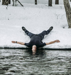 Man lies on back in snow spread eagle with head underwater in river person