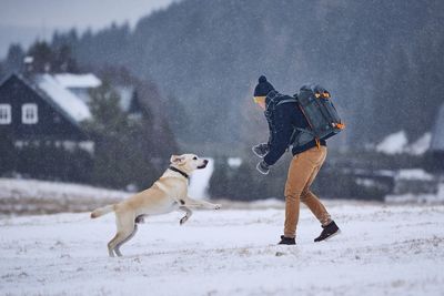 Side view of man playing with dog on field during snowfall