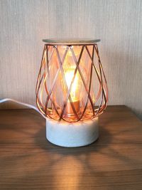 Close-up of illuminated lamp on table against wall