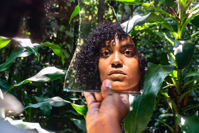 Cropped hand of woman holding mirror in forest