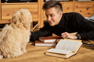 Man with dog holding book while lying on floor