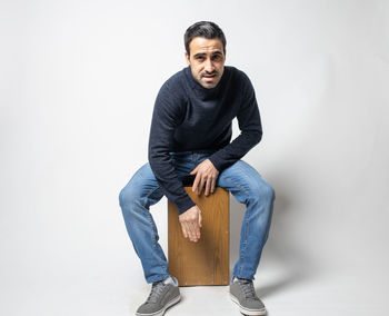 Portrait of young man sitting against white background