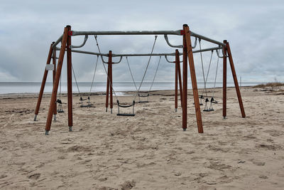 Empty swing on beach against sky