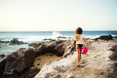 Rear view of woman standing at beach against sky