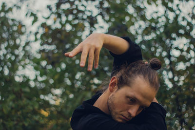 Thoughtful young man dancing while standing against trees 