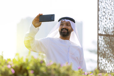 Smiling man in traditional clothing taking selfie with smart phone against clear sky