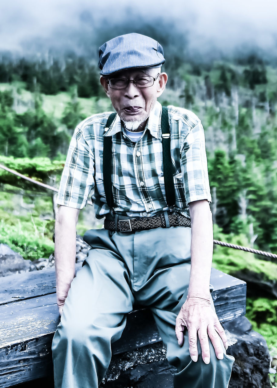 one person, real people, sitting, leisure activity, lifestyles, casual clothing, front view, focus on foreground, day, young men, men, nature, young adult, males, three quarter length, adult, water, cap, outdoors, contemplation