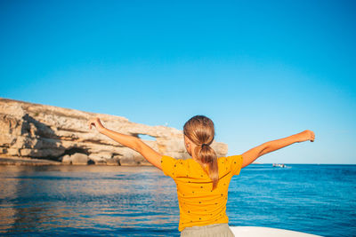 Rear view of woman standing by sea against clear blue sky