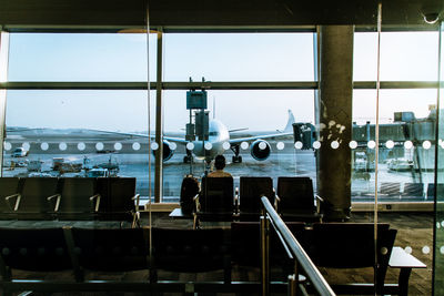 Man sitting in waiting area of airport and overlooking aircraft through glass window