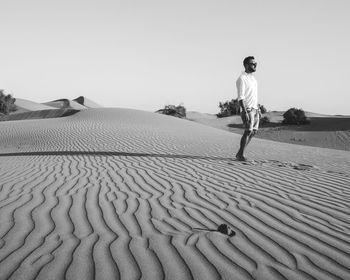 Man standing on sand dune against clear sky