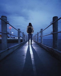 Rear view of woman standing on pier over sea against sky