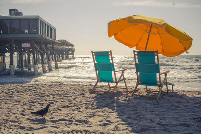 Deck chairs on beach against sky during sunset