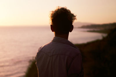 Rear view of man looking at sea during sunset