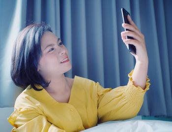 Young woman using mobile phone while relaxing on bed at home