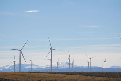 Windmills by snowcapped mountains against sky