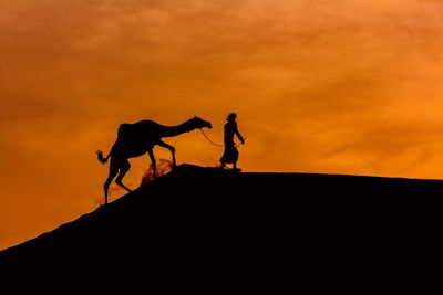 Silhouette men walking against orange sky