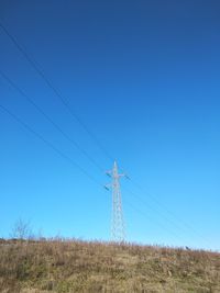 Low angle view of electricity pylon on field against clear blue sky