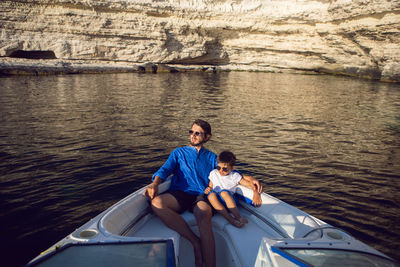 Father and son swim on the bow of a high-speed motor boat in the summer near  rocky coast in crimea