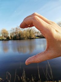 Hand showing love sign in lake against sky