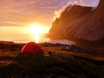 Tent on mountain by sea against sky during sunset