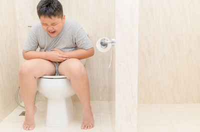 Boy with hands on stomach sitting in toilet