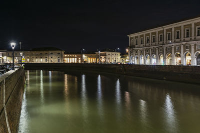 Bridge over river by illuminated buildings in city at night