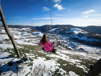 Woman in a rope swing on top of the mountains during winter with a beautiful panoramic view