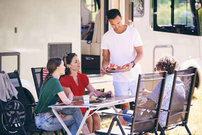 Man serving watermelon slices to family while camping at trailer park