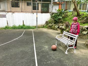 Senior woman looking at basketball while standing by bench at park
