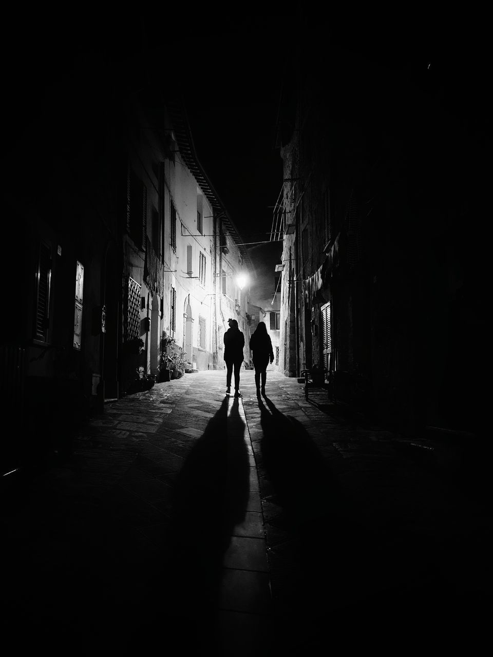 SILHOUETTE PEOPLE WALKING ON ALLEY AMIDST BUILDINGS IN CITY