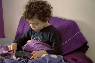 Sweet 4-5 year old boy with curly hair in bed awake in the morning, watching cartoons on tablet. 