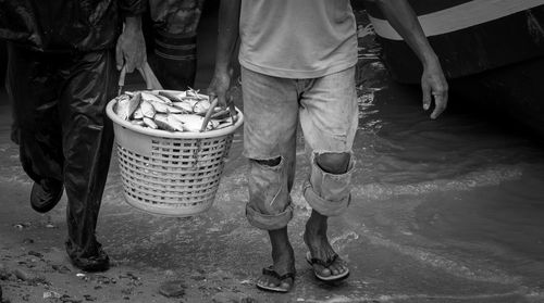 Low section of men carrying fish basket while walking at sea shore