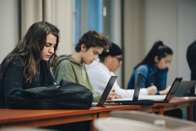 Teenage students using laptop at desk in classroom