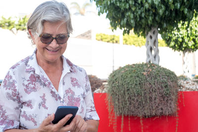 Smiling senior woman using mobile phone while standing outdoors