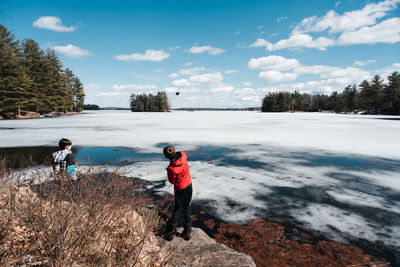 Two boys throwing rocks onto the ice on a lake on a spring day.